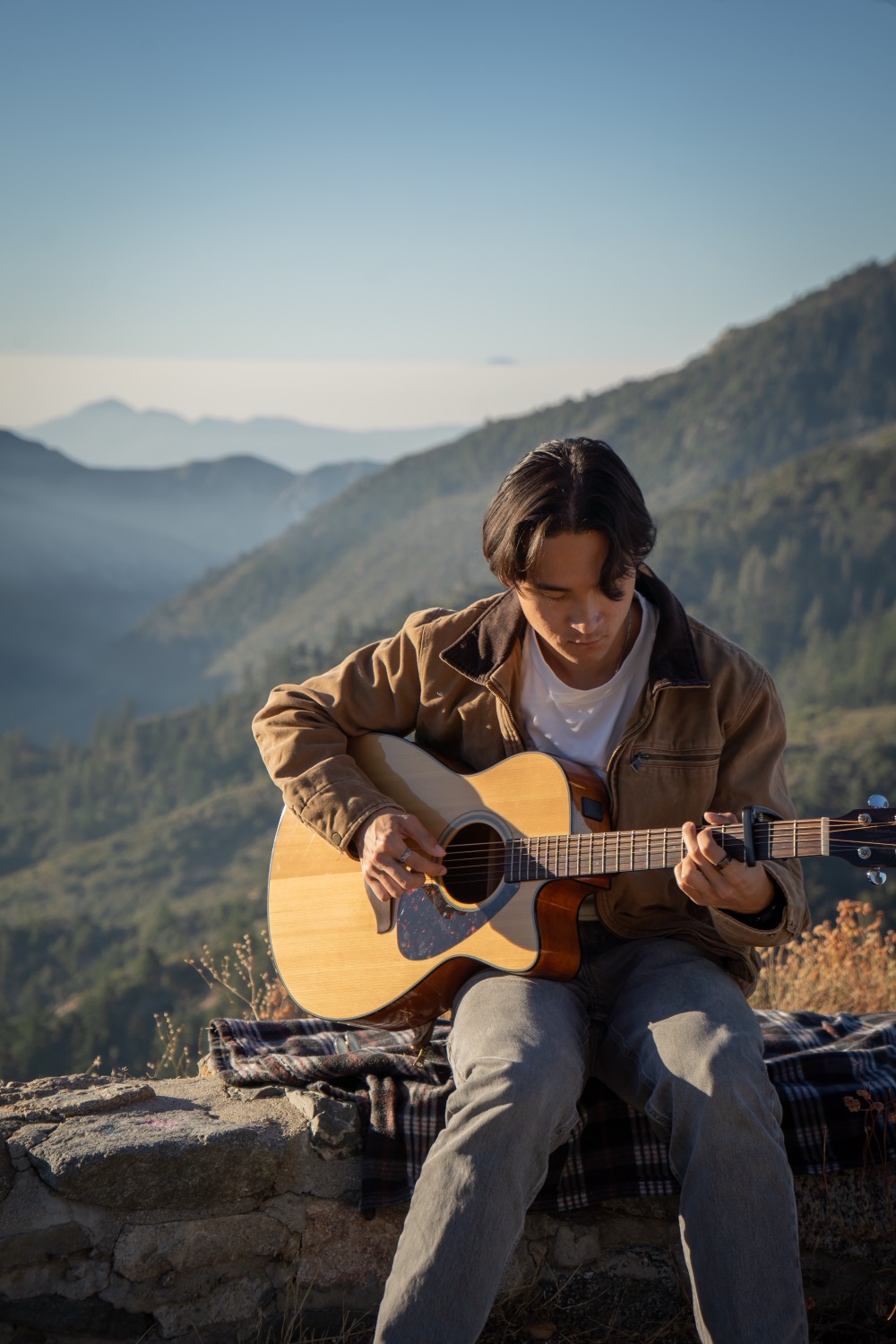 Playing guitar on a rock wall with mountains behind