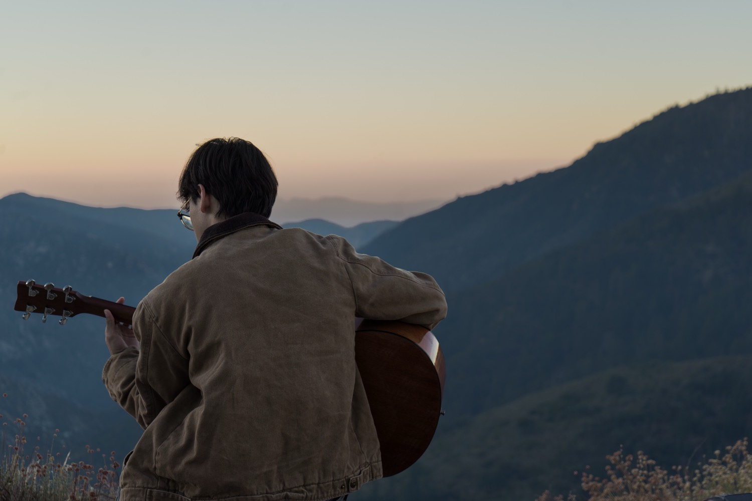 Playing guitar on a ridge at dusk over the mountains